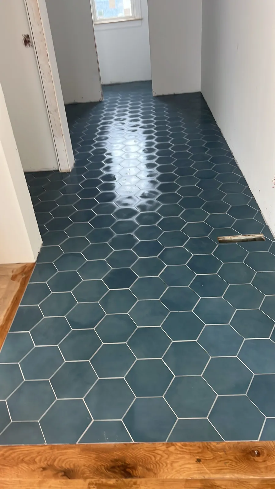 Room with newly installed dark blue hexagonal tile flooring and a wood border at the entrance. There is a window in the background and a floor vent on the right side.