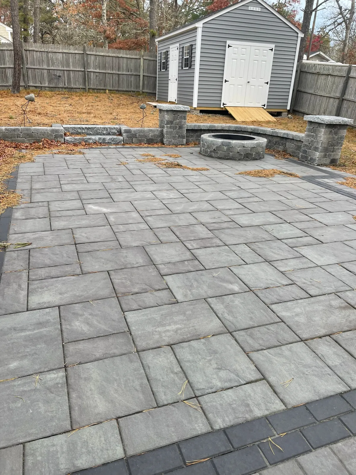 Stone patio with fire pit and shed in fenced backyard