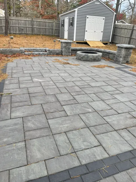 Stone patio with fire pit and shed in fenced backyard