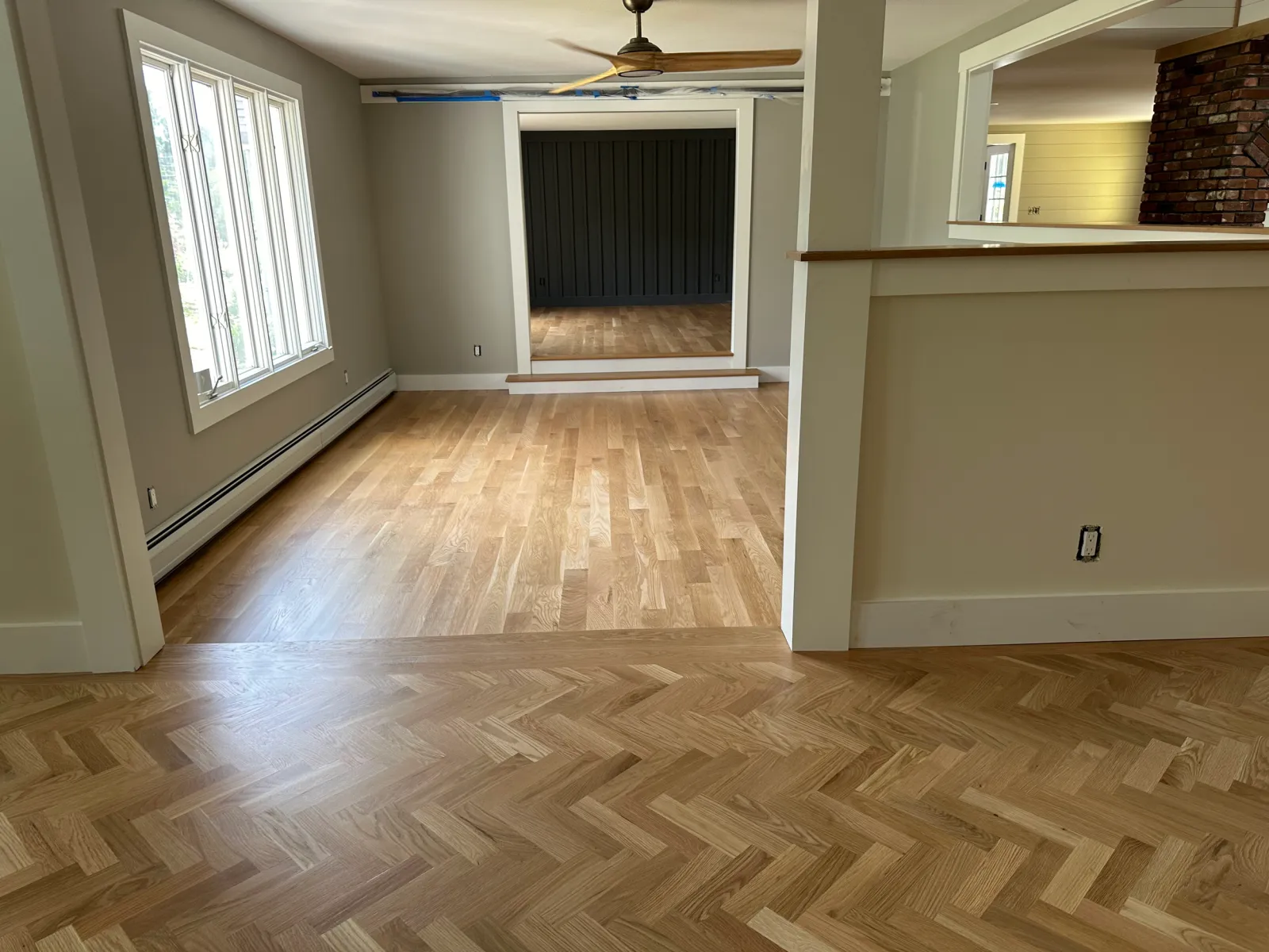 Empty room with wood flooring, a window with white trim, a black sliding door, and a partial brick fireplace wall.