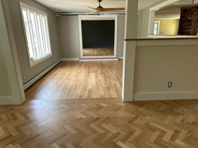 Empty room with wood flooring, a window with white trim, a black sliding door, and a partial brick fireplace wall.