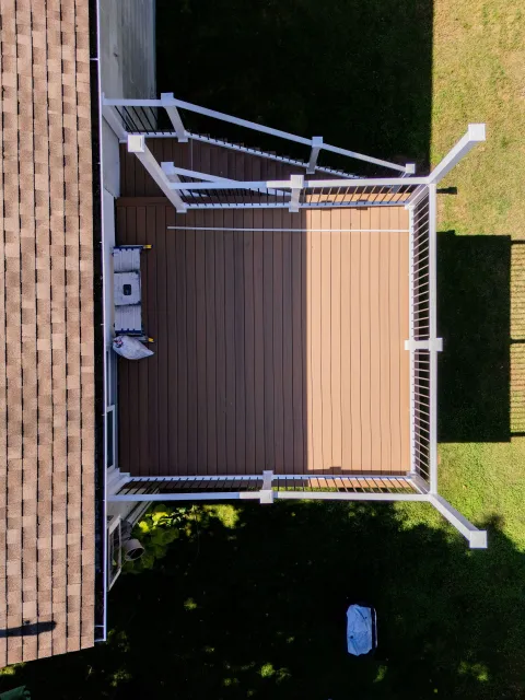 Overhead view of a deck with white railings, brown decking, and a portion of a house with a brown roof.