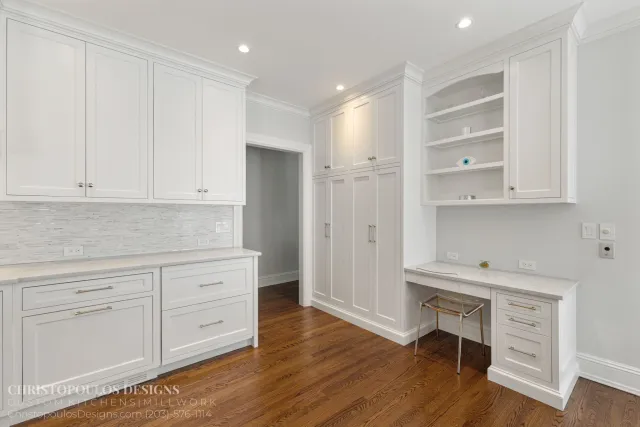 Modern kitchen with white cabinets, hardwood flooring, marble countertops, and a built-in open shelf with decorative items.