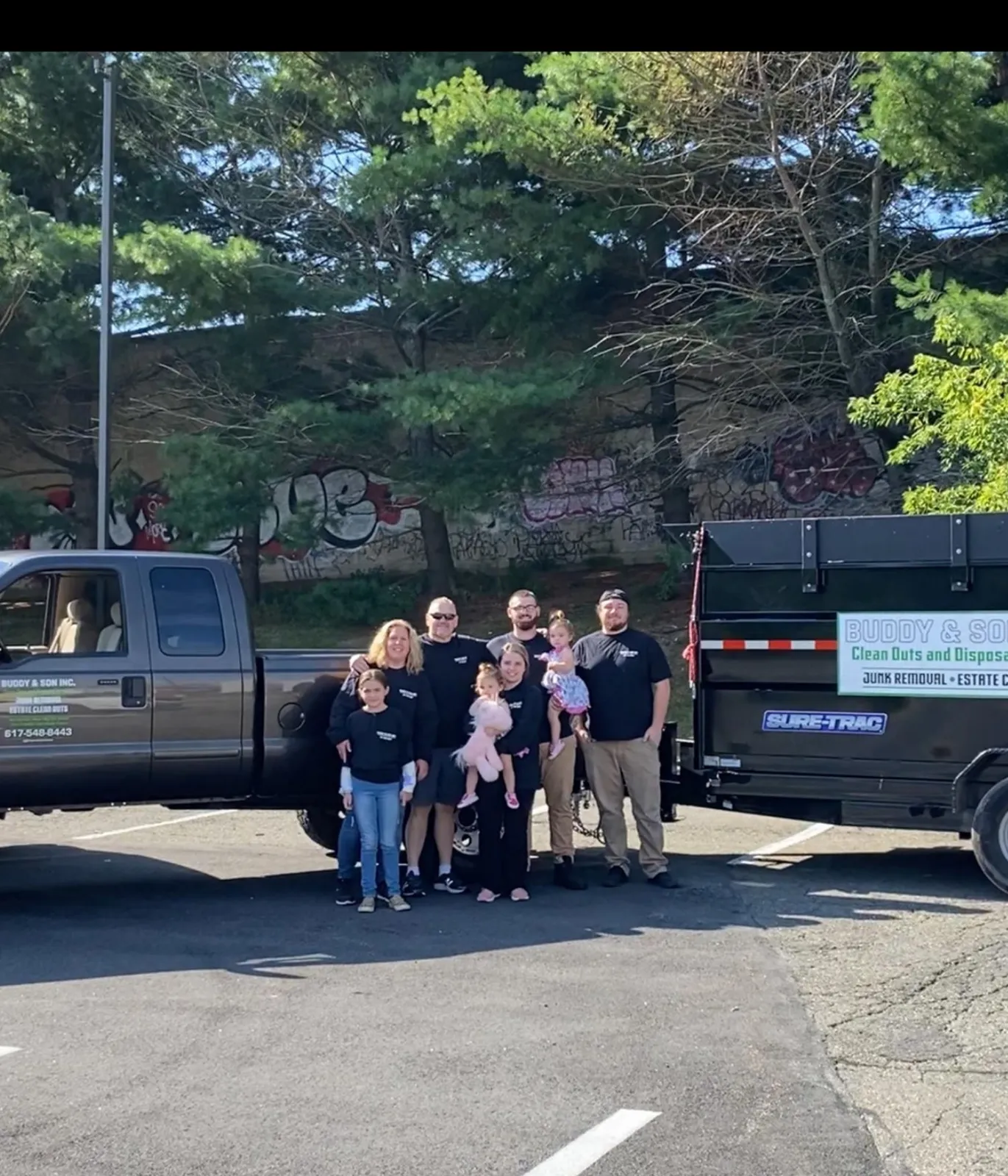 The Buddy & Son Cleanouts family standing in front of a gray with with a trailer