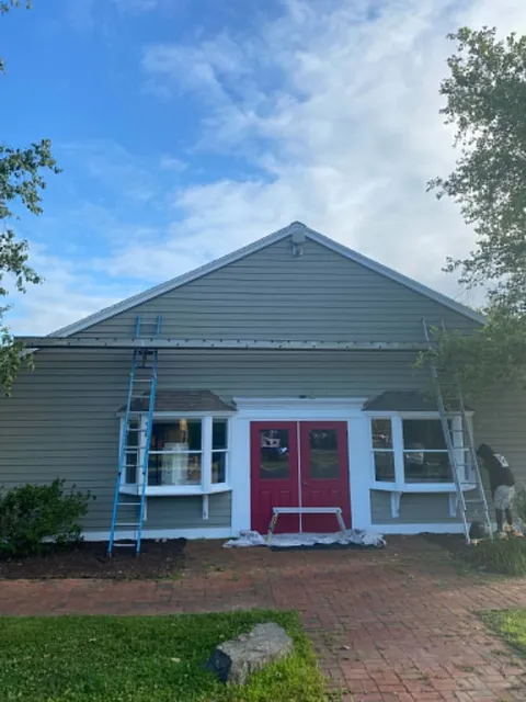 Late stage: the same storefront with new sage-green lap siding, white trim and red entry doors, ladders still up