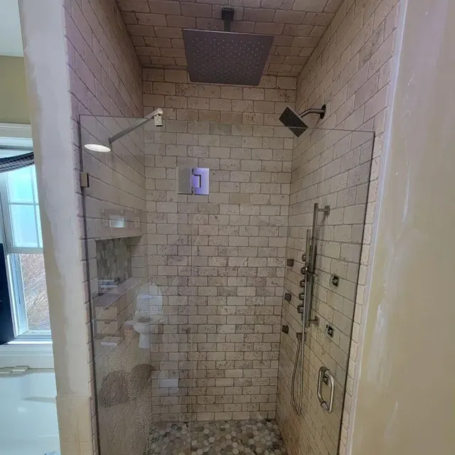 Tiled walk-in shower with glass door, rainfall showerhead, and built-in shelves.