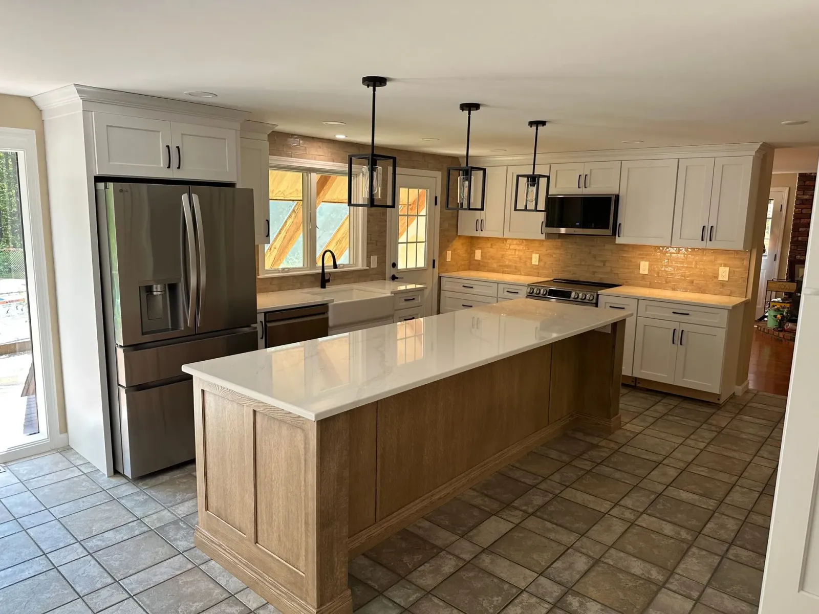 Modern kitchen with a large island, stainless steel fridge, tiled floor, and white cabinets