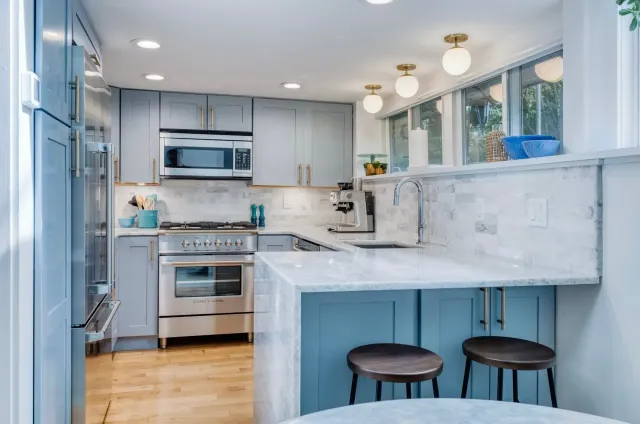 Bright white kitchen with marble island, stainless steel appliances, and two stools by the counter.