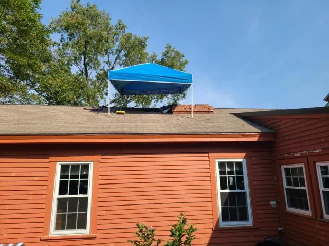Blue canopy on a roof, supported by white poles. Red building with windows, blue sky.