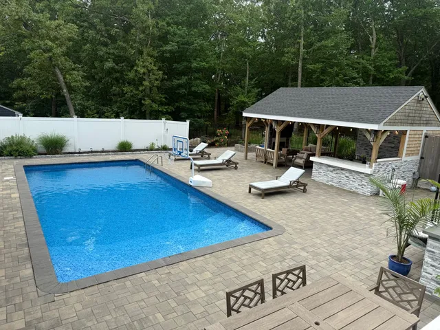 Paver patio surrounding an in ground pool with a stone faced pool house and bar