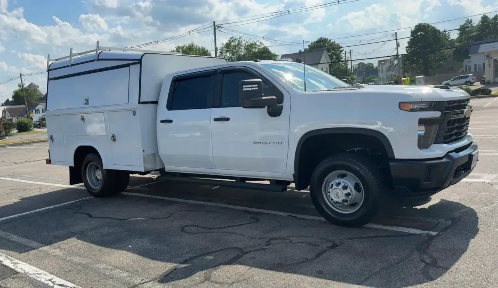 A white Chevrolet crew cab utility truck with a service body and storage compartments parked in an asphalt lot.