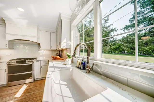 Bright kitchen with white cabinets, large window overlooking greenery, and farmhouse sink.