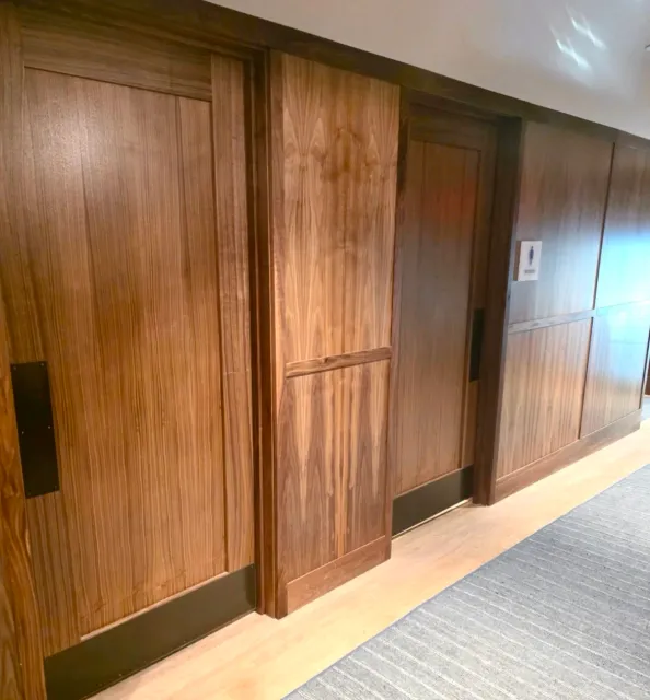 Wooden wall with sliding door and a restroom sign on the right side. wall paneling , custom wall paneling,  walnut paneling