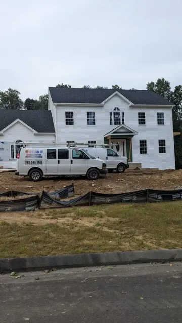 A white van is parked in front of a large white house under construction.