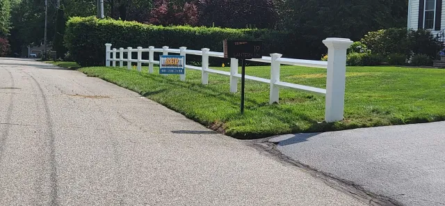 White fence lining a grassy roadside beside a paved path on a sunny day