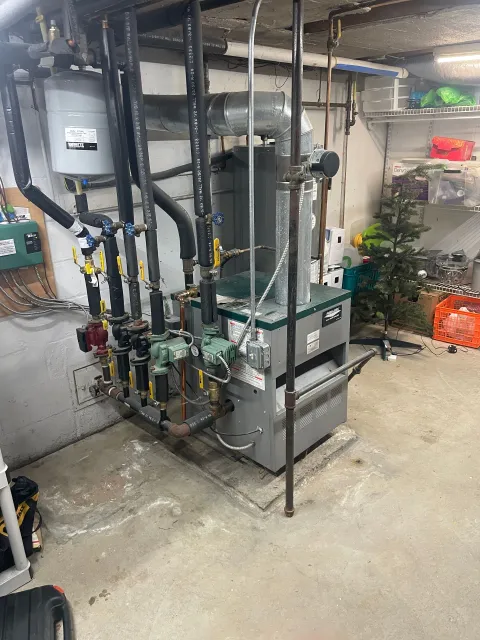 Basement boiler and plumbing equipment with pipes, valves, and utility tanks in a utility room