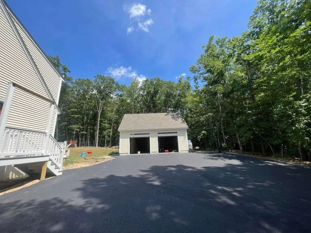 Asphalt driveway and garage with trees in background