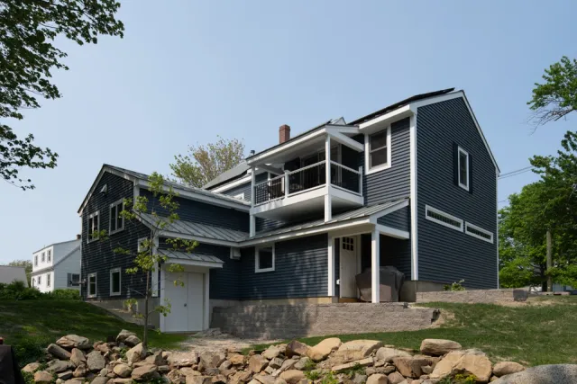 Dark blue house with white trim, a balcony, and rock landscaping.