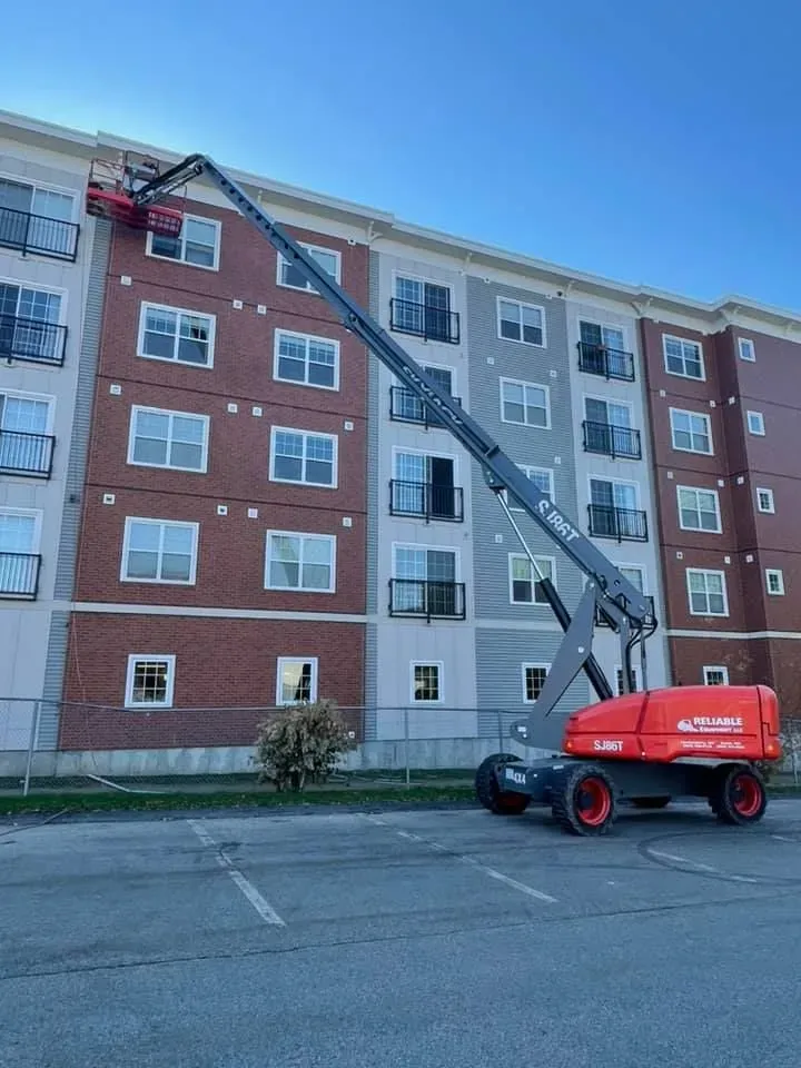A cherry picker lifts a person near an apartment building. The cherry picker is red and gray.