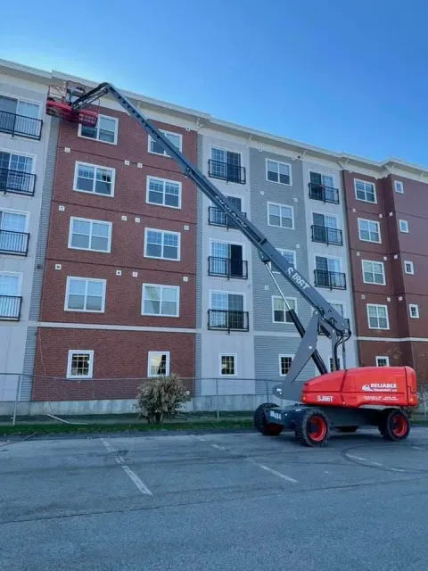 A cherry picker lifts a person near an apartment building. The cherry picker is red and gray.