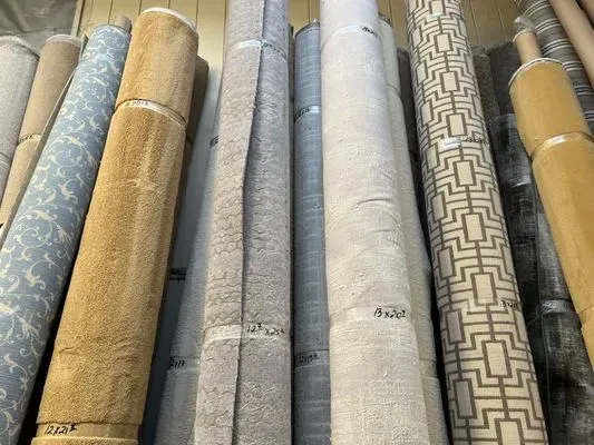 Rolls of various carpets, beige and patterned, stacked in a store.