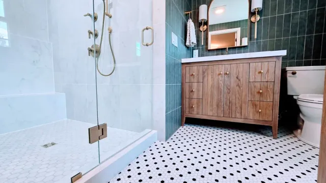 Modern bathroom remodel in Glastonbury, CT with glass shower, white tile floor, and wooden vanity with mirror.