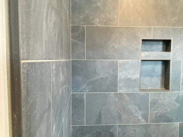 A close up of a shower wall with tiles and a shelf.