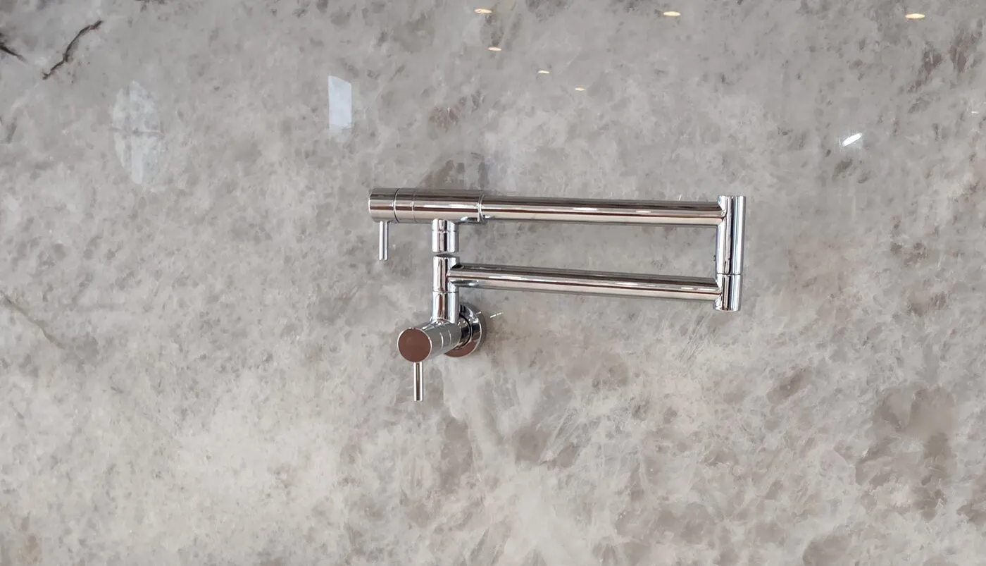 Wall-mounted folding pot filler faucet installed over a stone backsplash