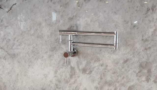 Wall-mounted folding pot filler faucet installed over a stone backsplash