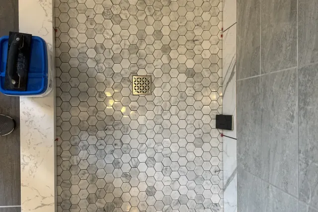 Marble hexagon mosaic shower floor bordered by large-format grey wall tile — custom tile work by Dmtilellc in Newington, CT