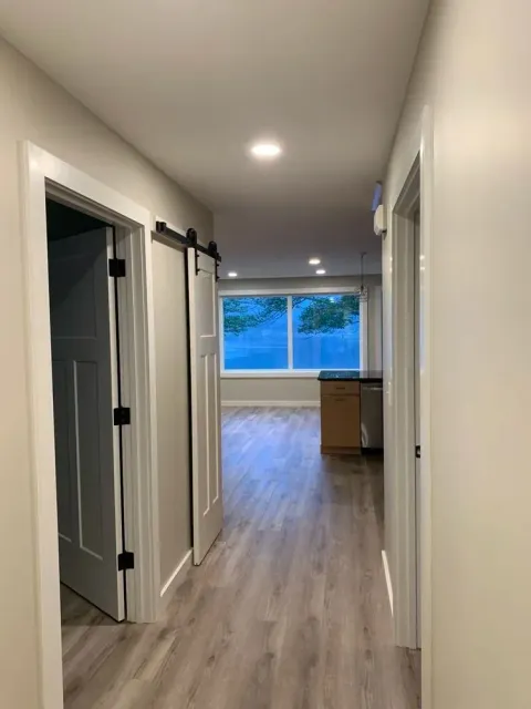 Hallway with wood floors, two white doors, one with a sliding barn door style. View to a kitchen.
