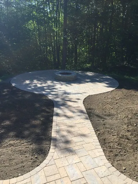 A brick walkway leading to a fire pit in the middle of a forest.