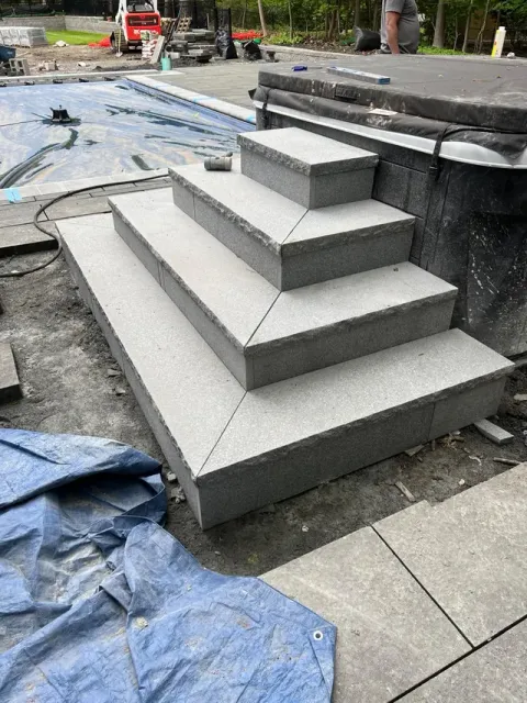 Gray stepped concrete platform under construction beside a walkway, with tools and tarps nearby