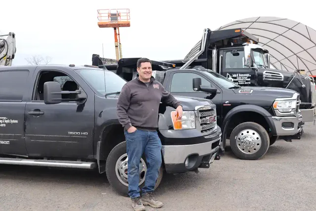 John Bensavage leaning on his GMC 3500HD work truck with additional vehicles in the background