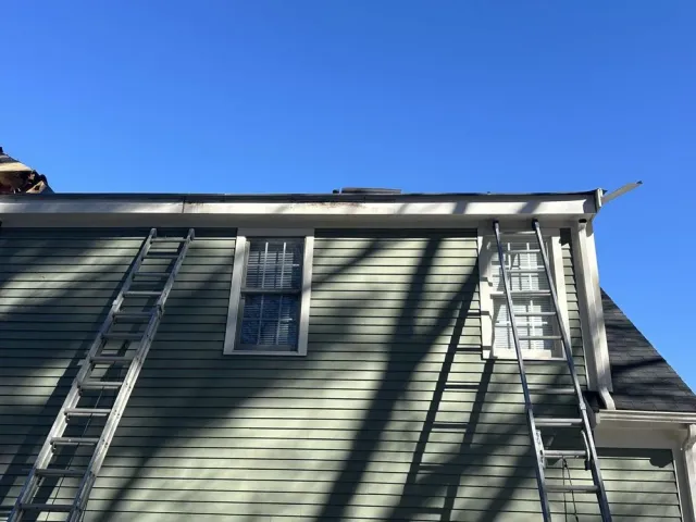House exterior with two ladders leaning against light green siding under a clear blue sky