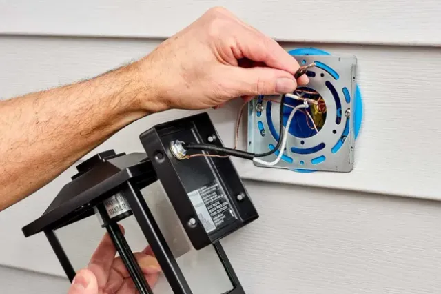 Electrician in blue shirt and cap working on a circuit breaker panel.