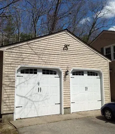 Two-car garage with white doors, light siding, and a dark roof; car parked to the right.