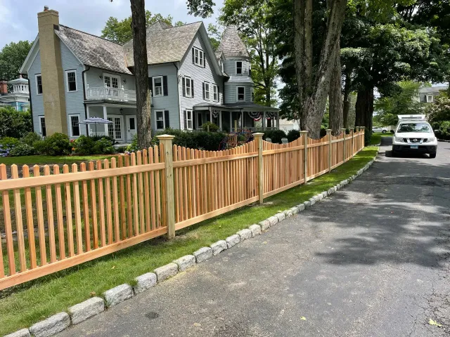 A wooden fence is along the side of a road next to a house.