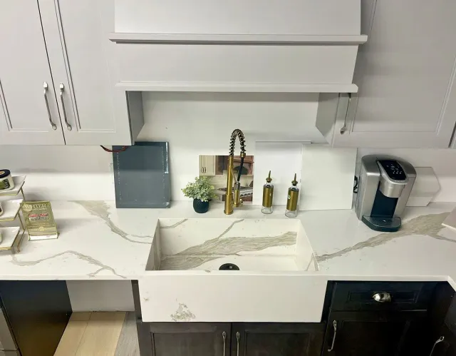 Kitchen with white countertops, sink, and cabinets, a gold faucet, and a Keurig coffee maker.