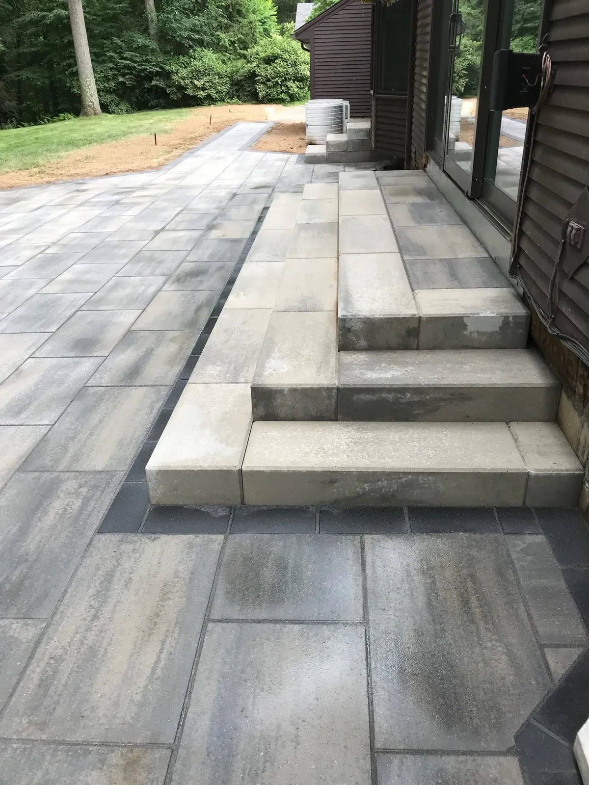 Paver patio and steps leading to a building with dark siding.
