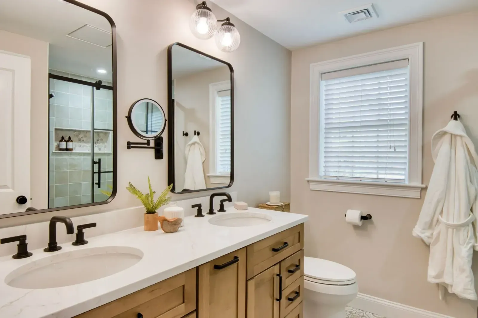 Bright bathroom with double sinks, mirrors, white walls, and tan vanity cabinets.