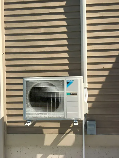 A daikin air conditioner is mounted on the side of a house