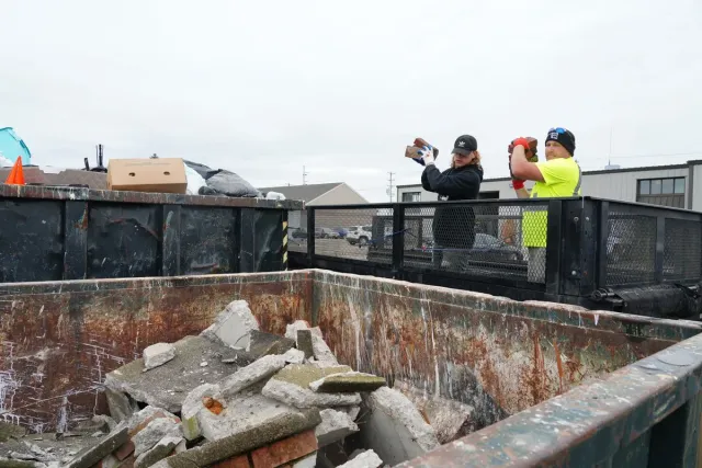 Two Dump Guy employees throwing chunks of concrete into the dump body of a dump truck