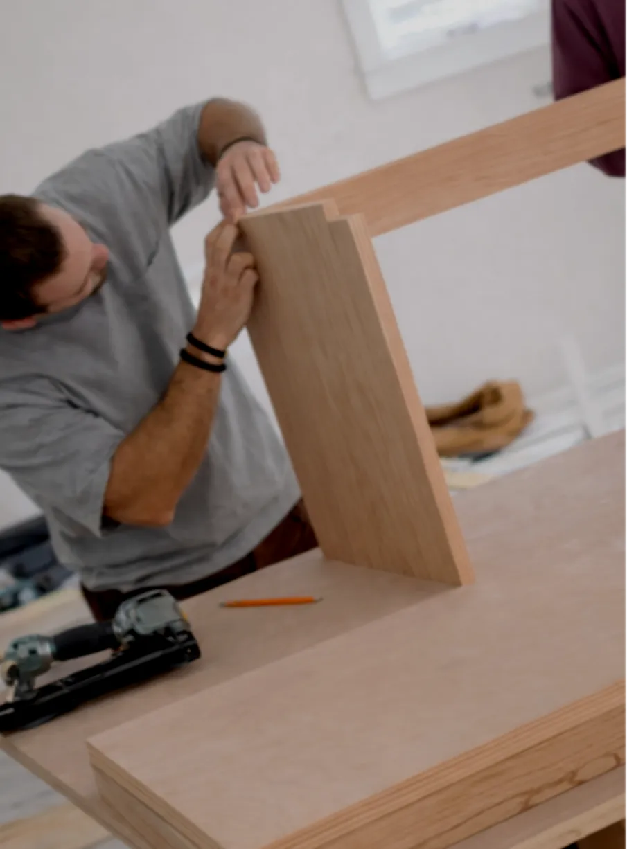A man assembling a wooden piece, possibly furniture, in a workshop.