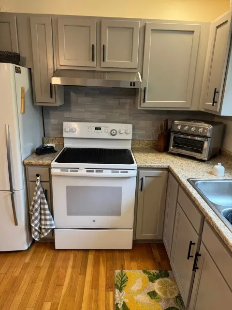 Kitchen with gray cabinets, white appliances, and light wood floors.