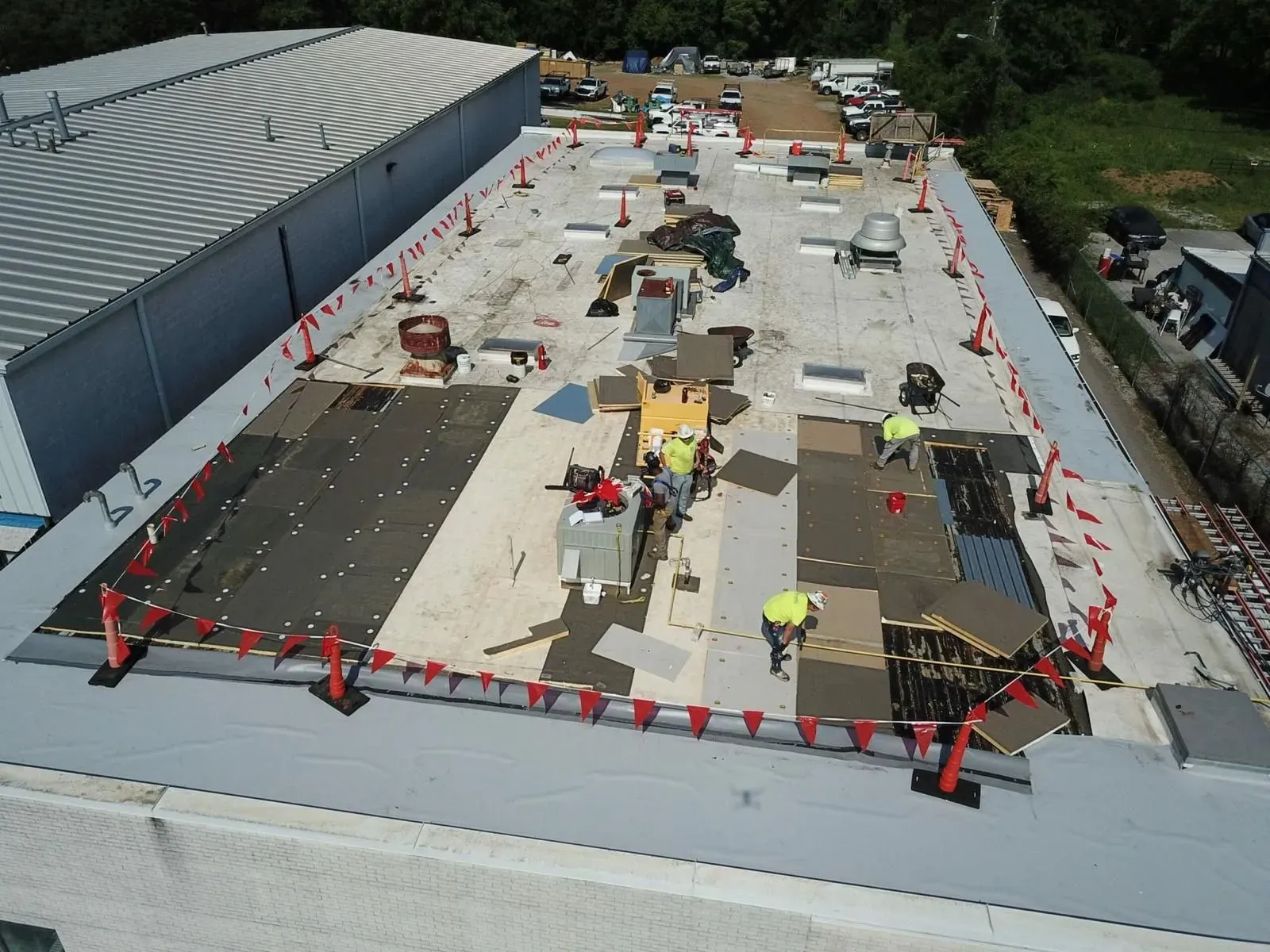 Aerial view of a rooftop construction site with workers, equipment, cones, and marked work zones.