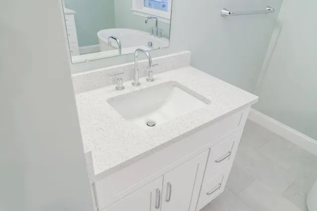 White bathroom vanity with sink, mirror, and light gray walls and floor.
