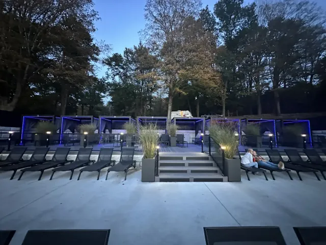 outdoor-poolside-lounge-with-multiple-cabanas-blue-lights-and-trees-at-dusk-in-ct