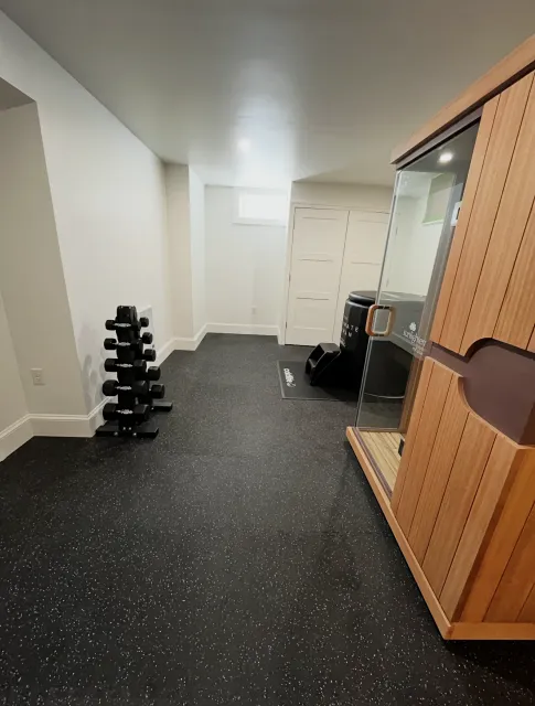 Empty gym room with black speckled floor, dumbbells, and wooden storage cabinet along the wall