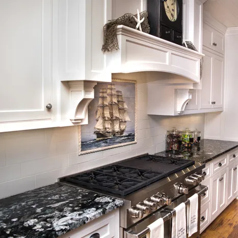 Kitchen with white cabinets, black and white granite countertops, and a stainless steel stove.